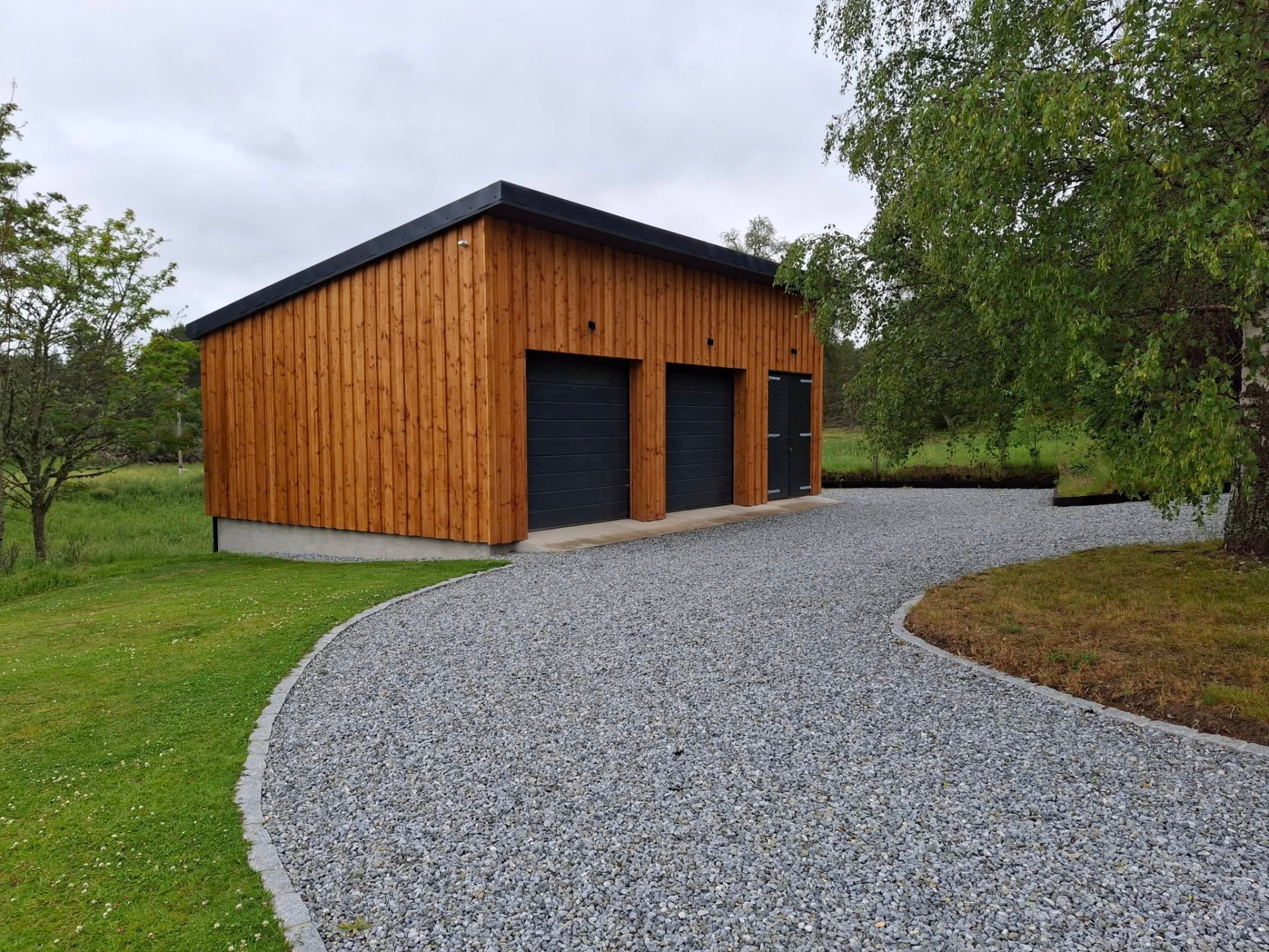 Custom timber-clad garage build with twin doors on a gravel driveway in Speyside